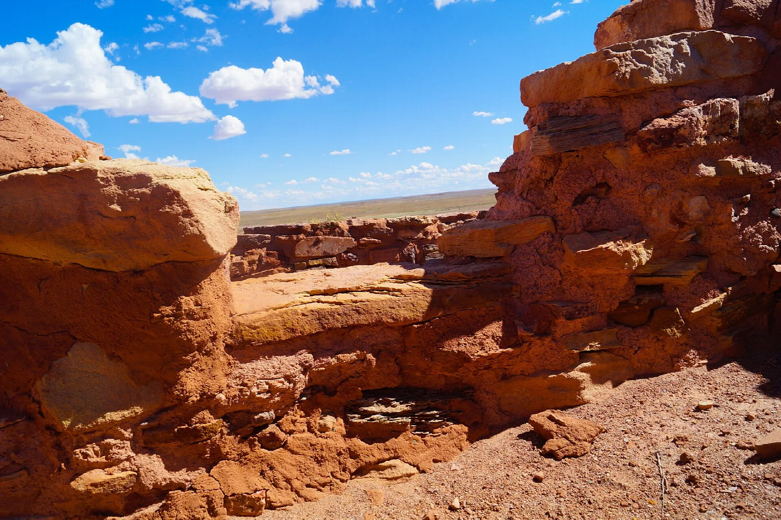 Weathered red sandstone ruins under a bright blue sky with clouds