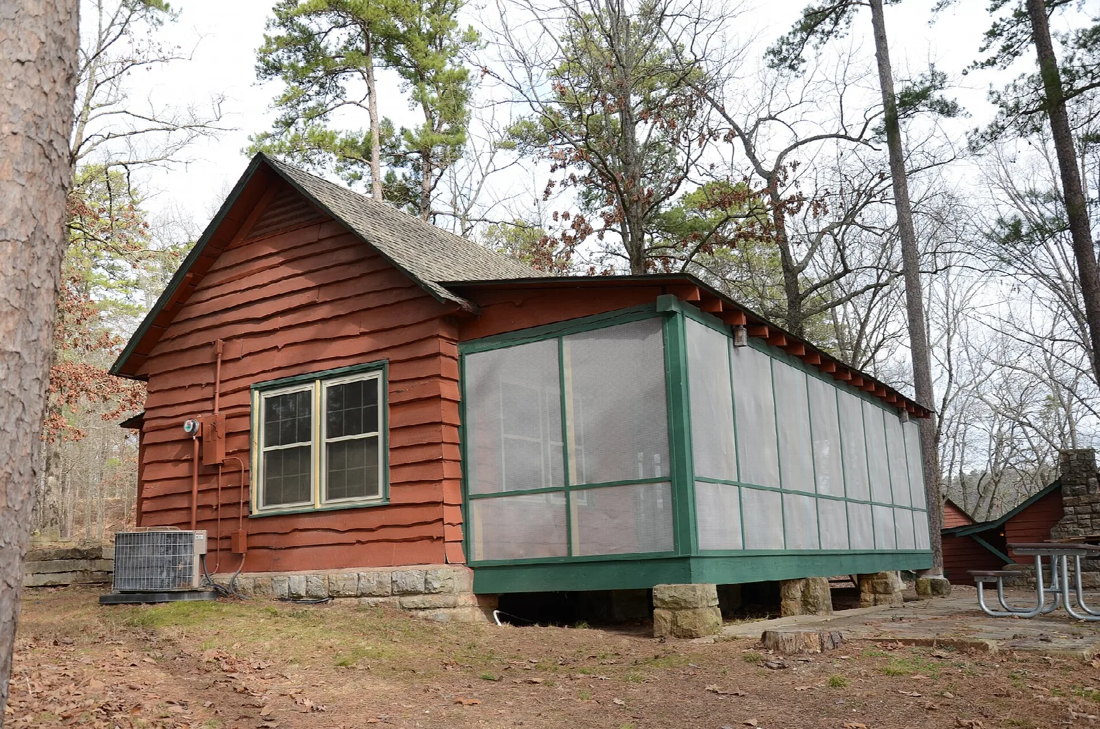 Red-brown cabin with a screened side porch among pines