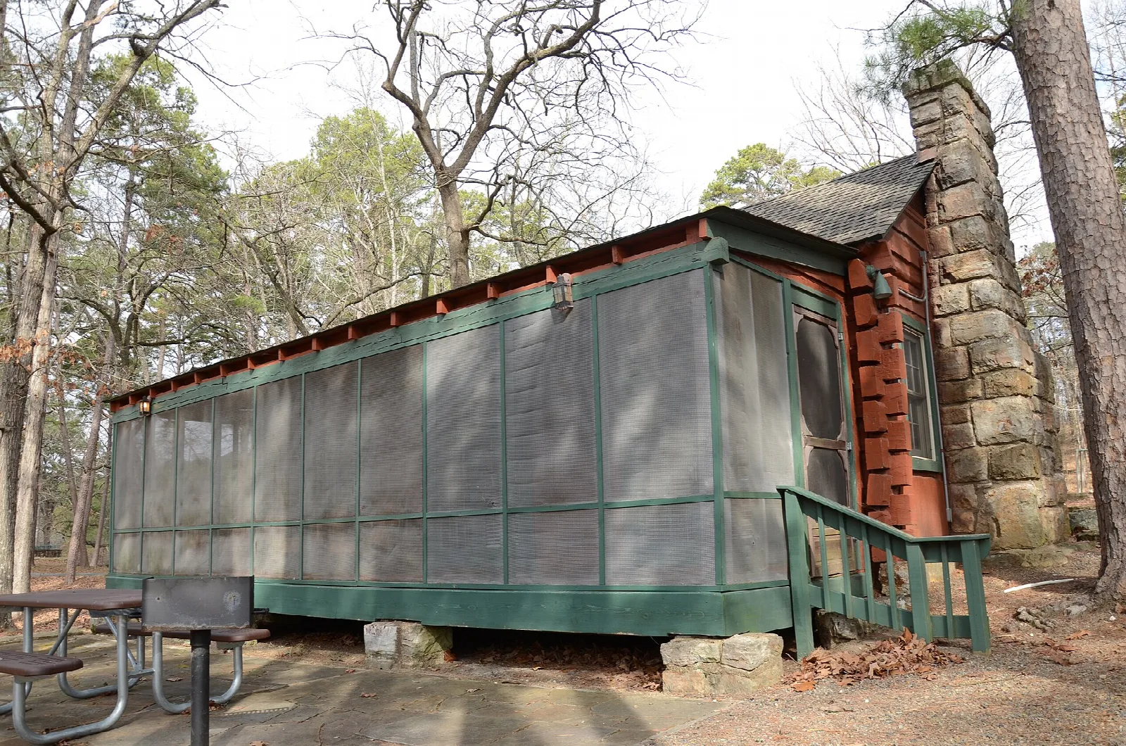 Wooden cabin with screened porch and a stone chimney among trees