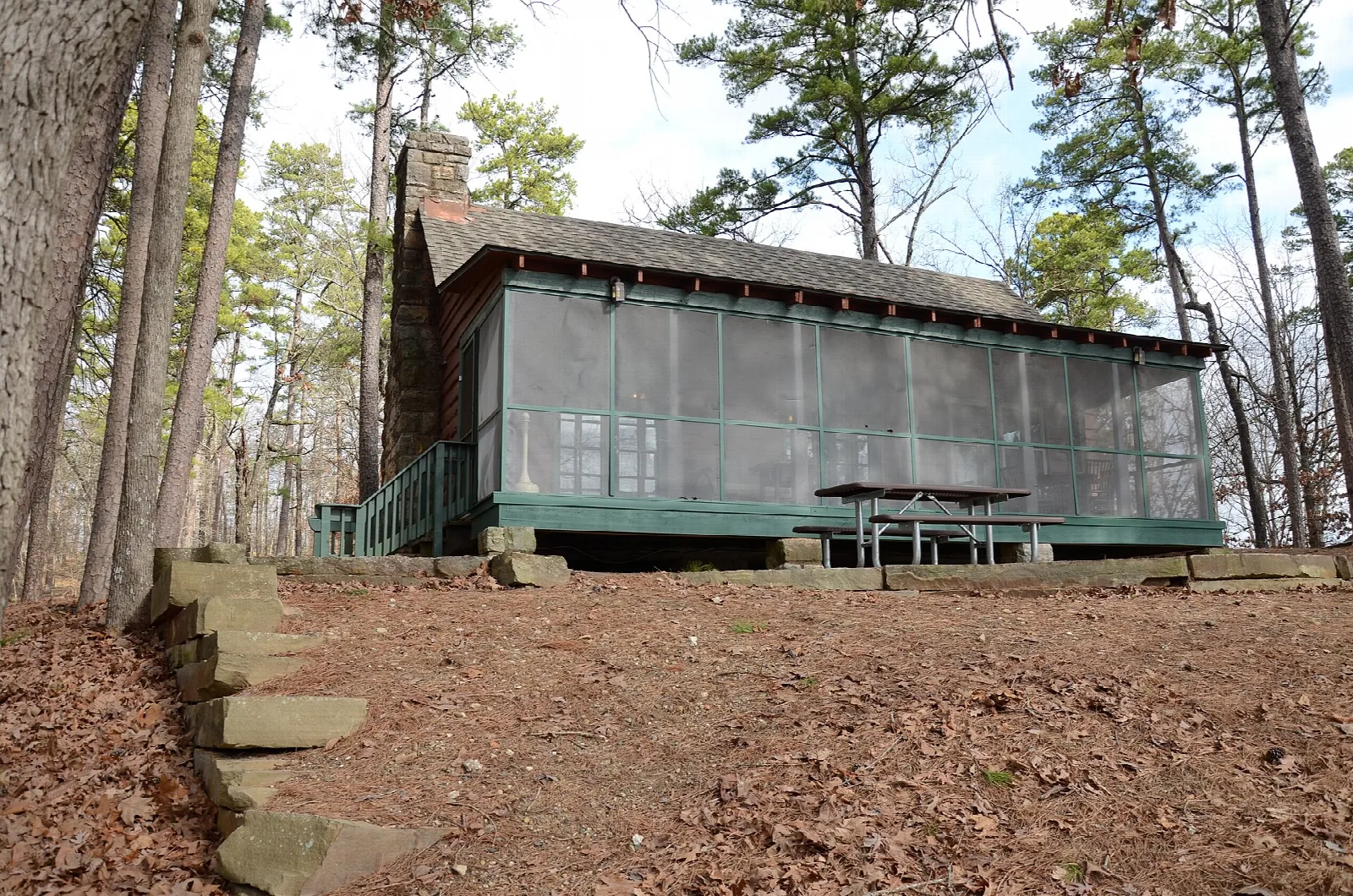 Green screened-in cabin with a stone chimney in bare winter woods