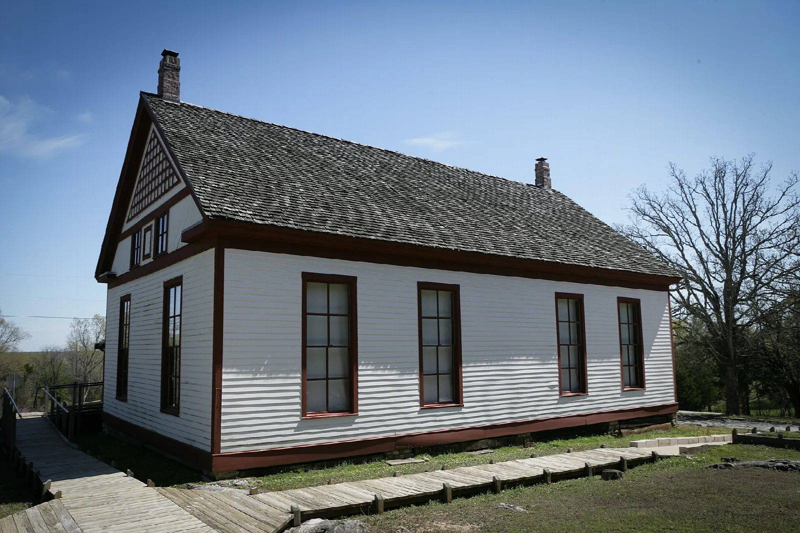 White one-room schoolhouse with a dark roof and a boardwalk beside it