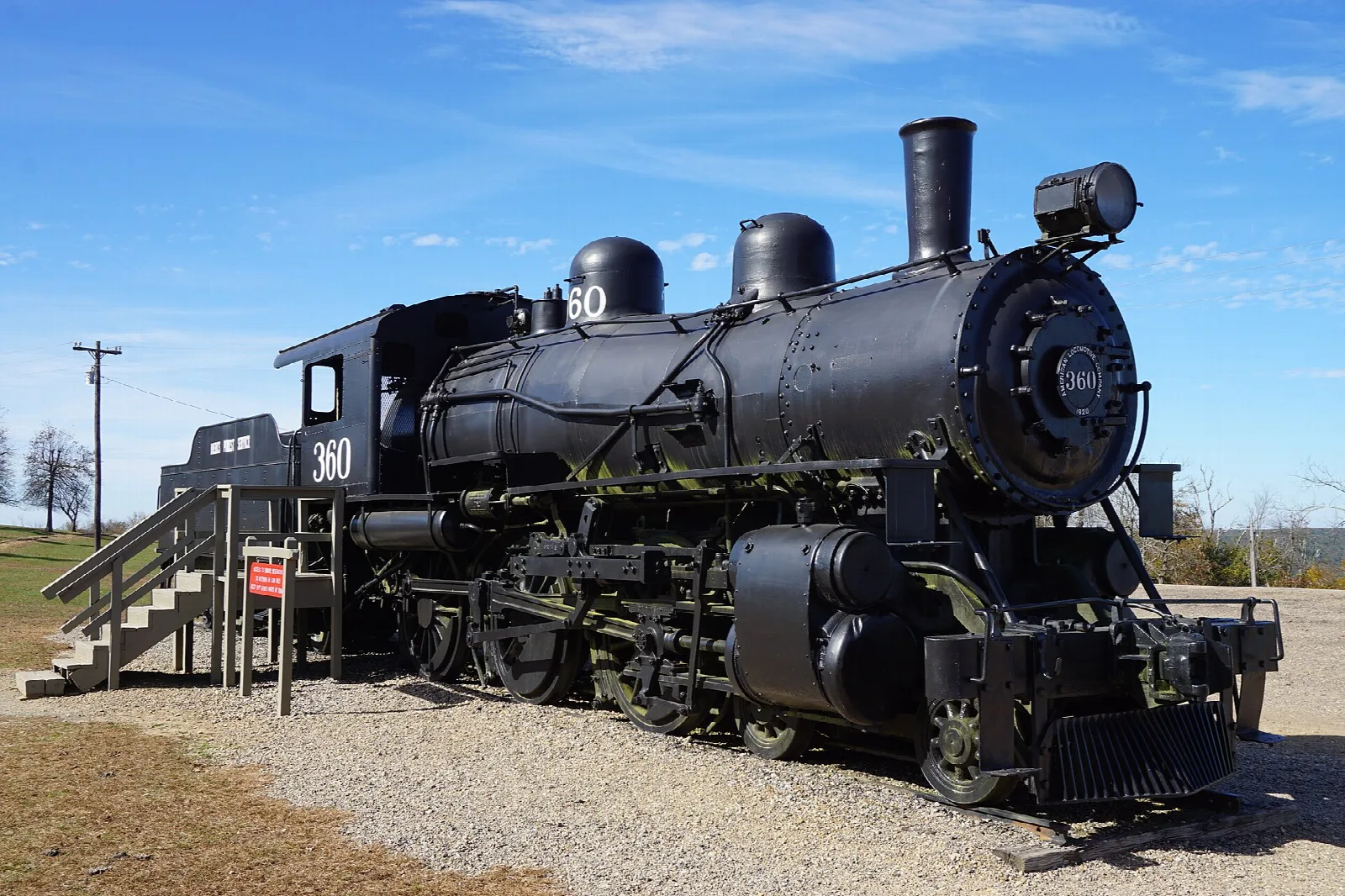 Black steam locomotive on display on a gravel pad under blue sky