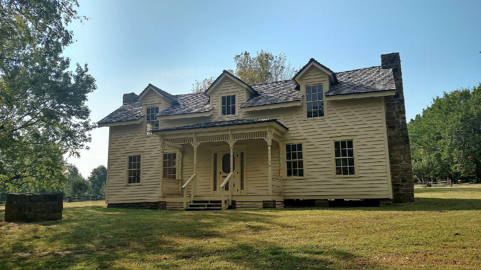 Two-story yellow farmhouse with a stone chimney on a mown lawn
