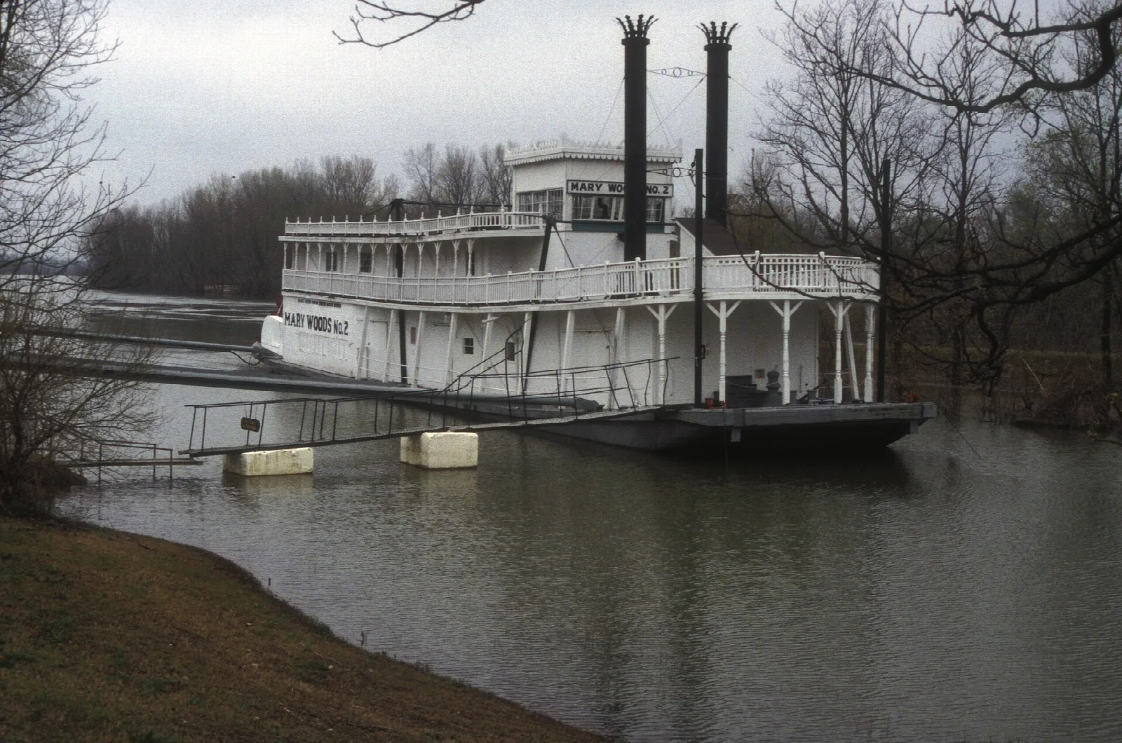 White steamboat with two smokestacks tied up on a gray river