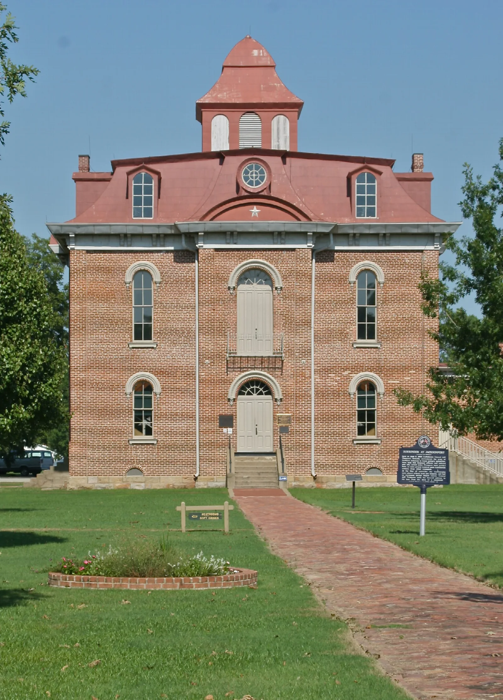Tall red brick courthouse with a cupola seen from a brick path