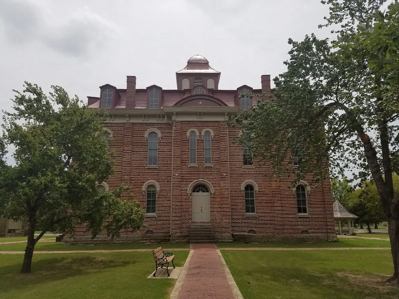 Red brick courthouse with a cupola behind a brick walkway and a bench