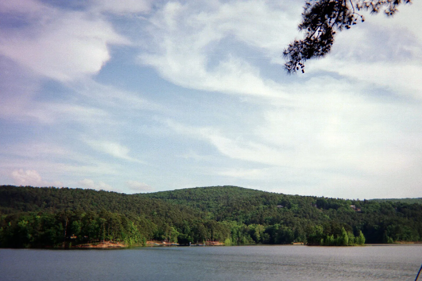 Forested hills across a wide lake under a wispy sky