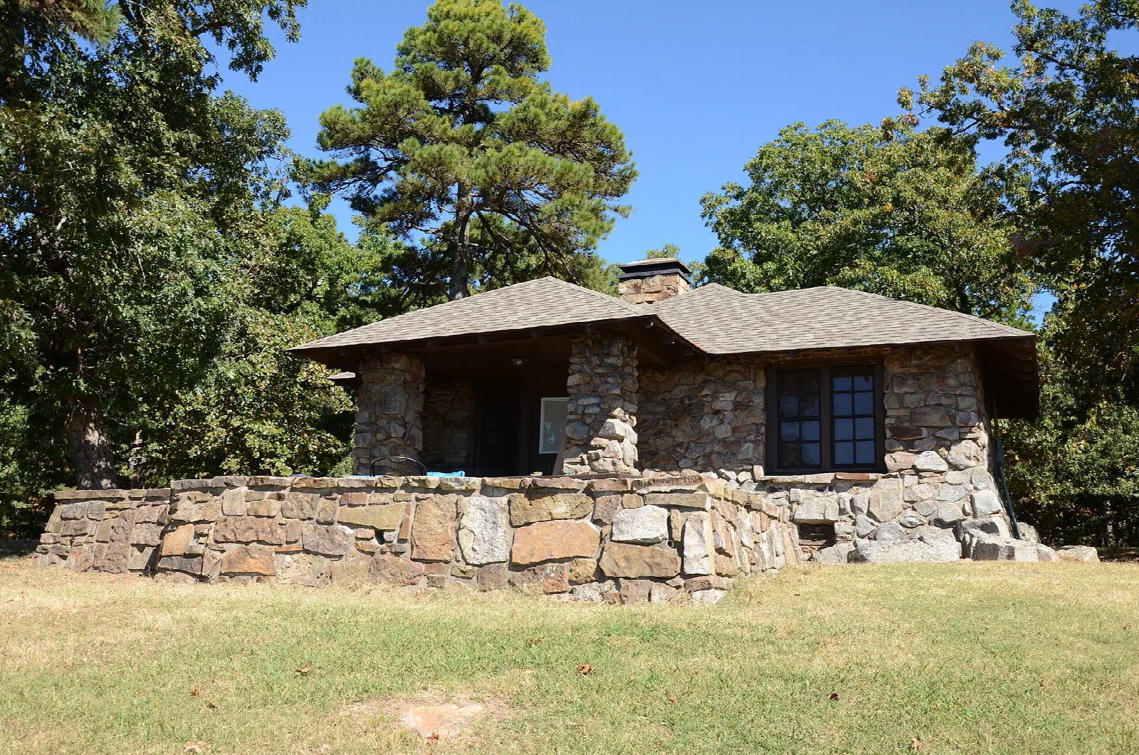 Low stone cabin with large windows on a grassy lot among trees