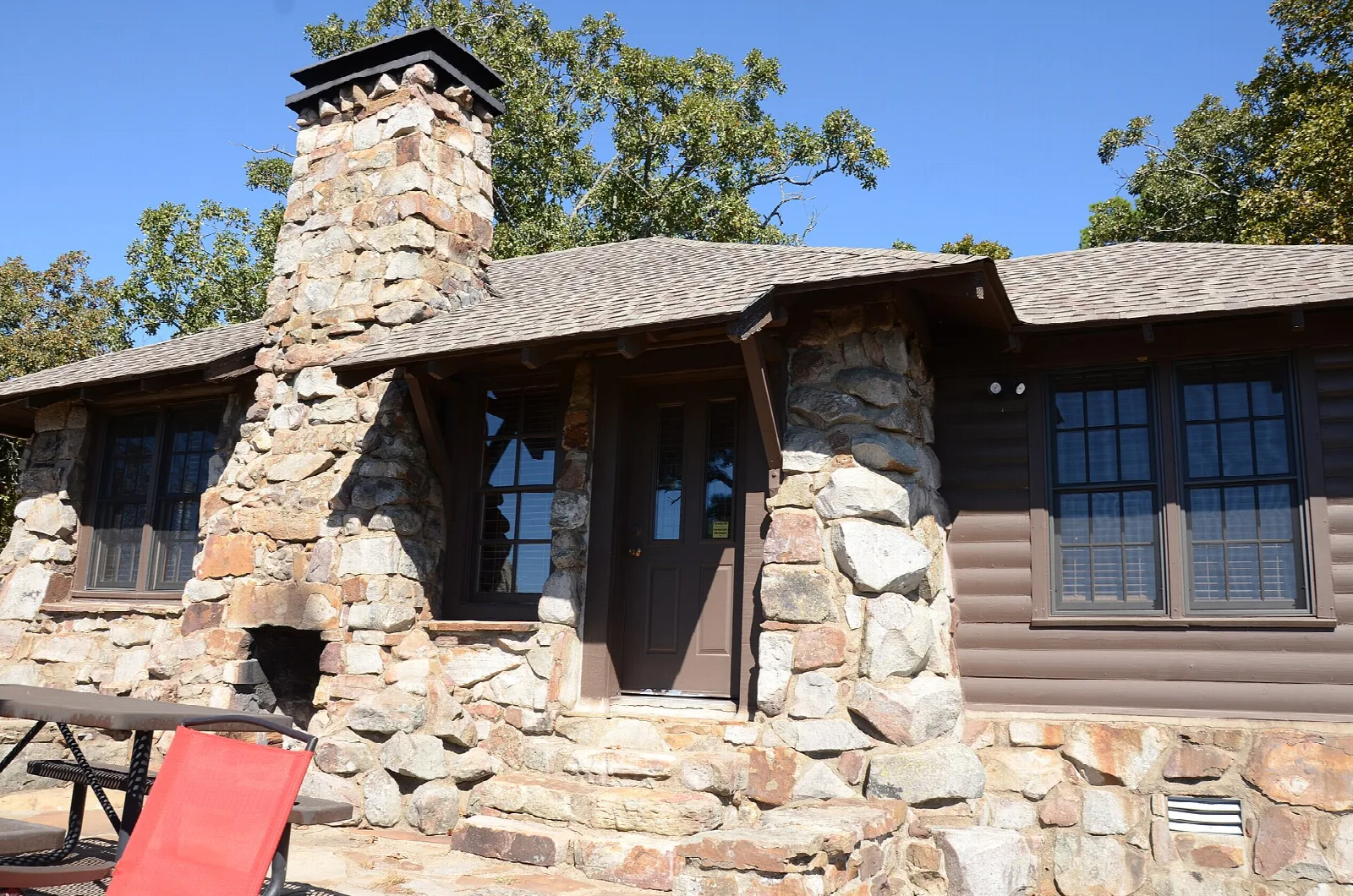 Stone cabin with a tall chimney and a red chair on the porch