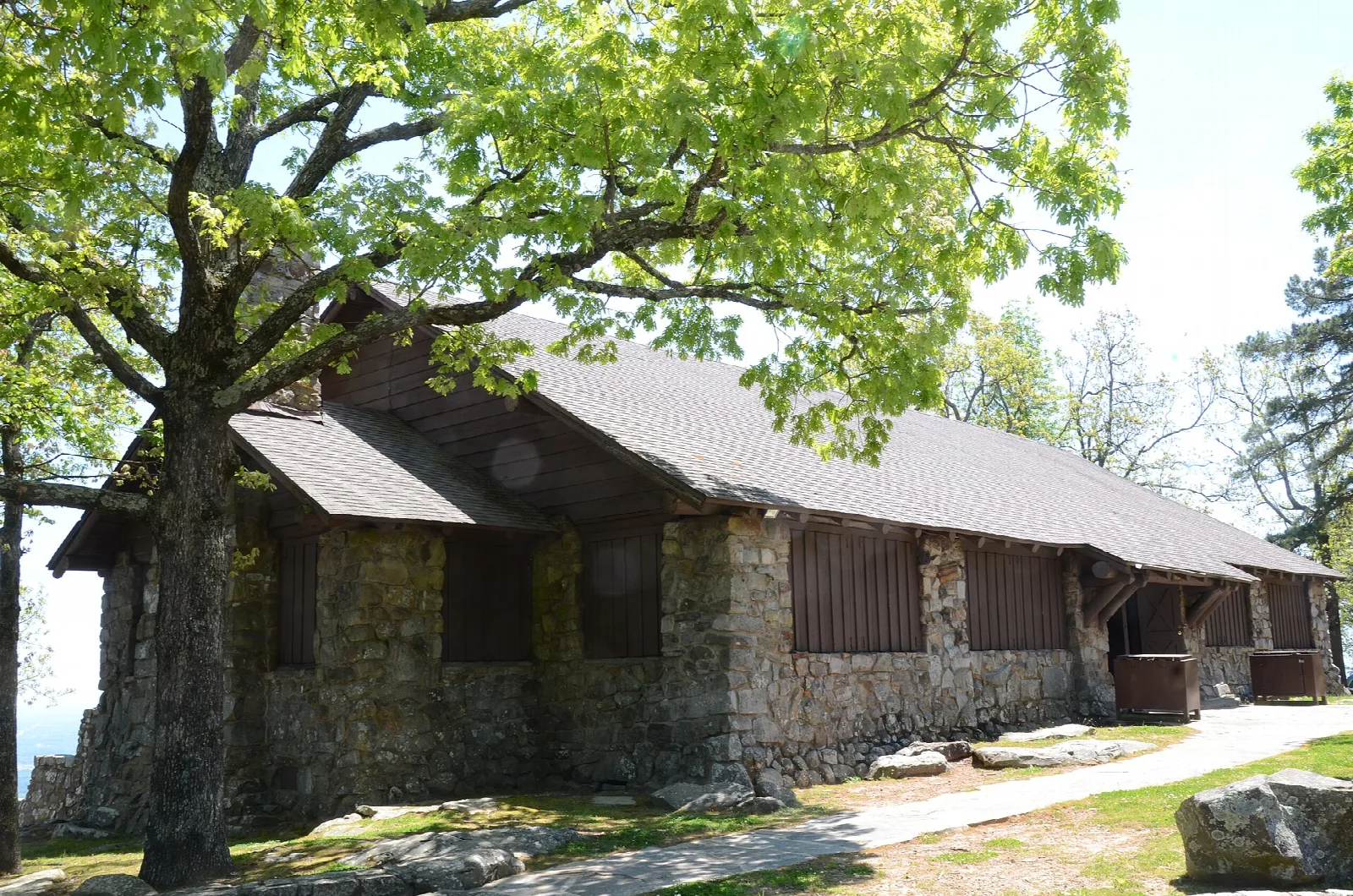 Rustic stone and timber pavilion beneath a large leafy tree