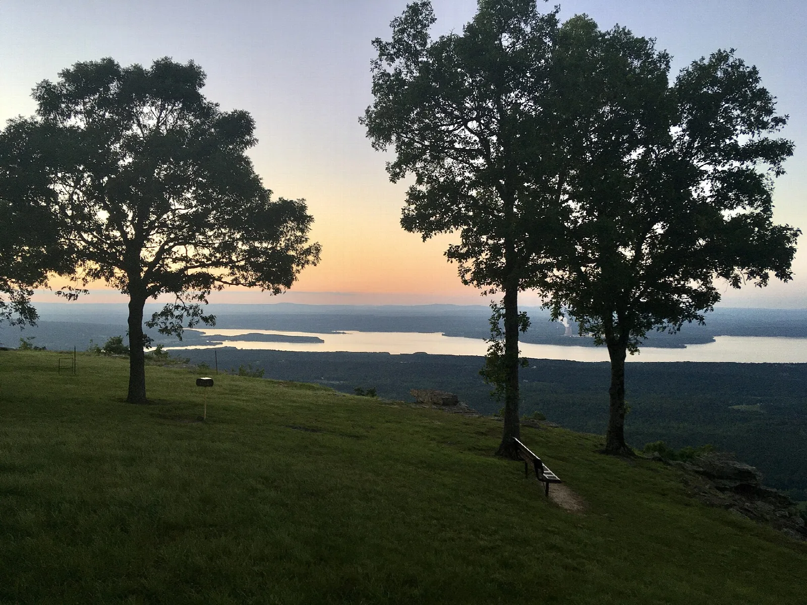 Trees on a grassy hilltop overlook with a lake far below at dusk