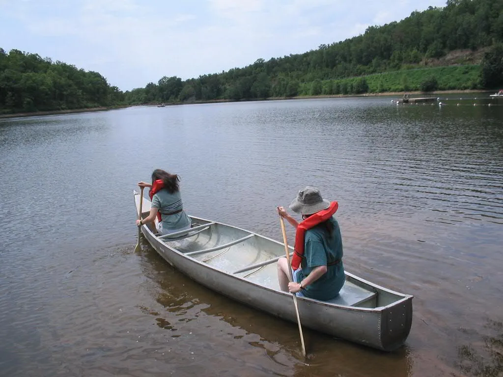 Two people paddling a canoe on a calm lake with tree-covered hills behind