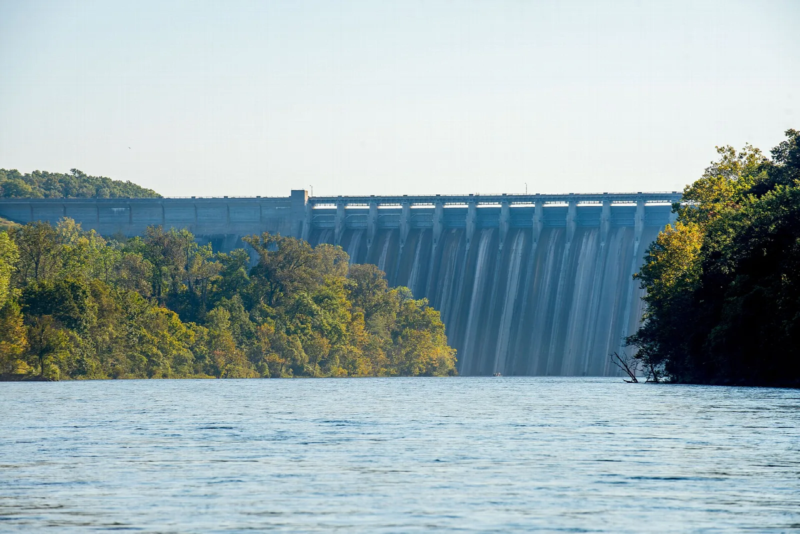 Long concrete dam holding back blue water with trees on both banks