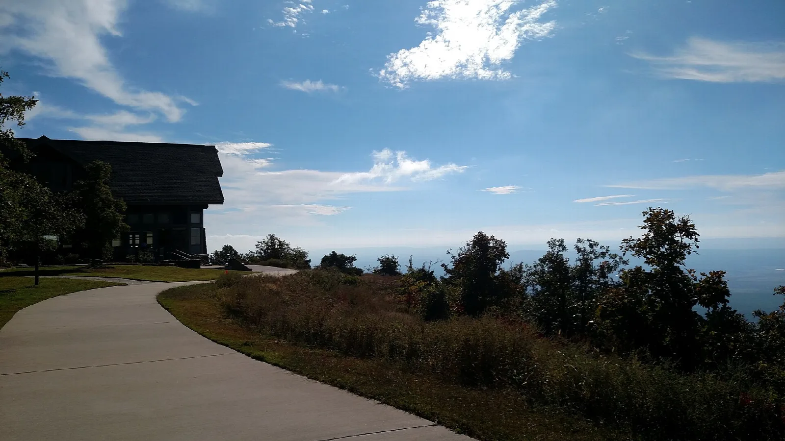 Paved walkway curving along the mountain edge toward a large dark building and blue sky