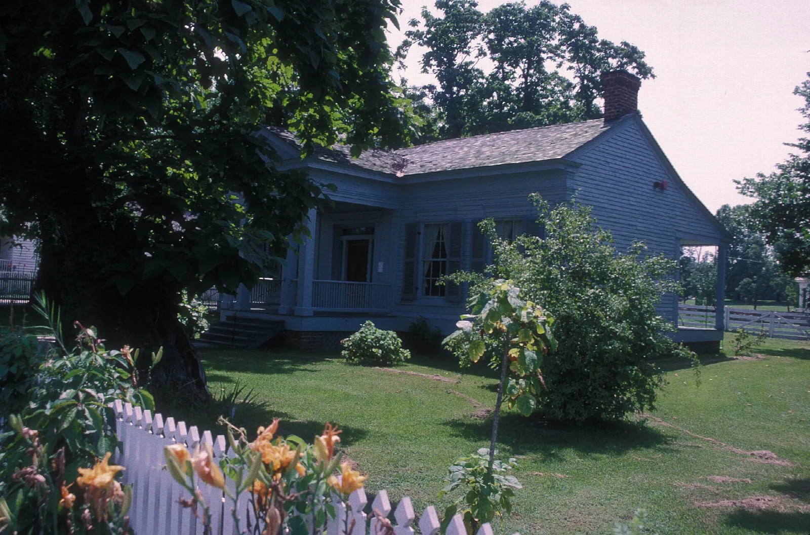 Greek Revival house with a white picket fence and flowers in front