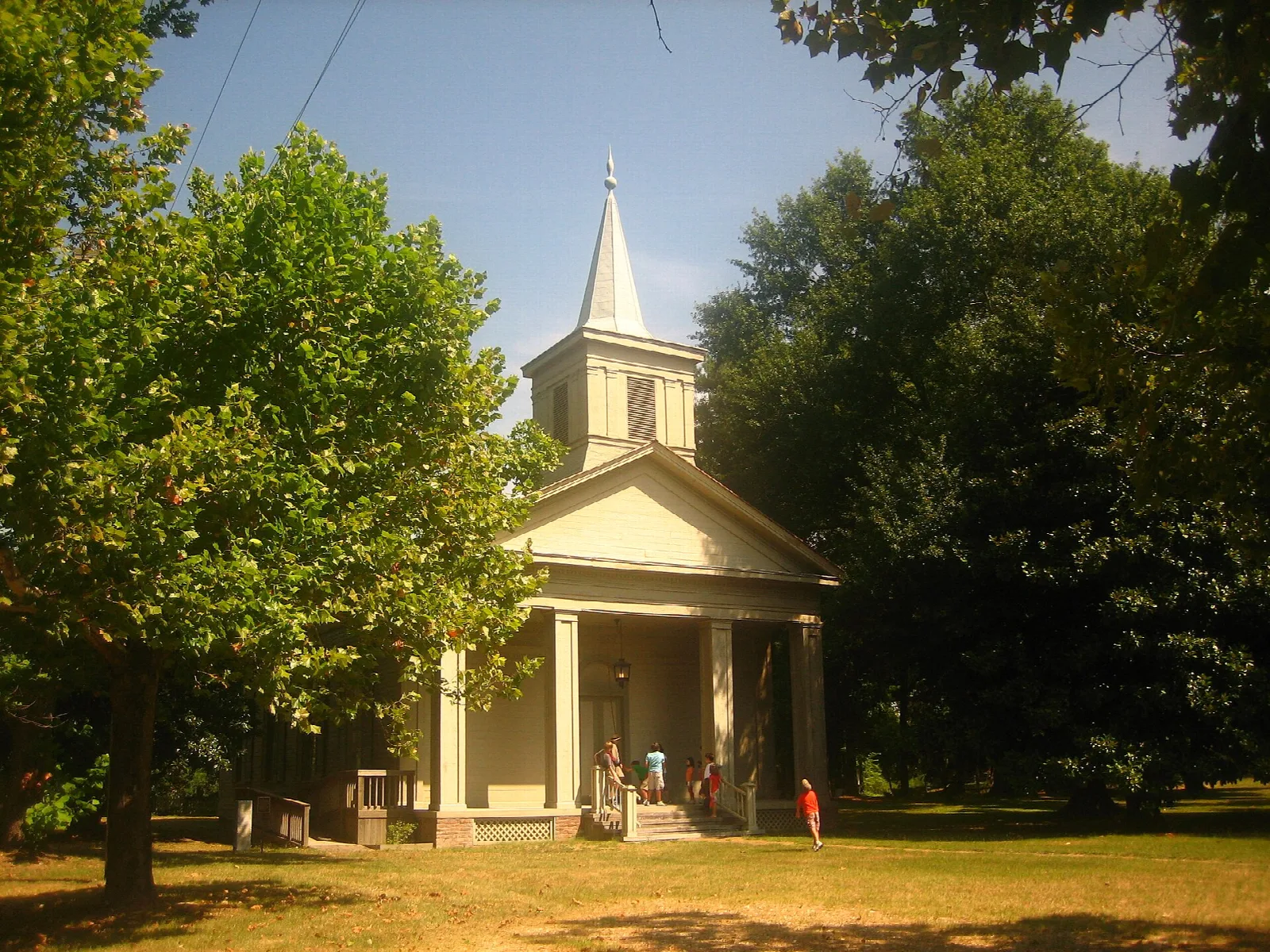 Small white church with a steeple and columned porch among trees
