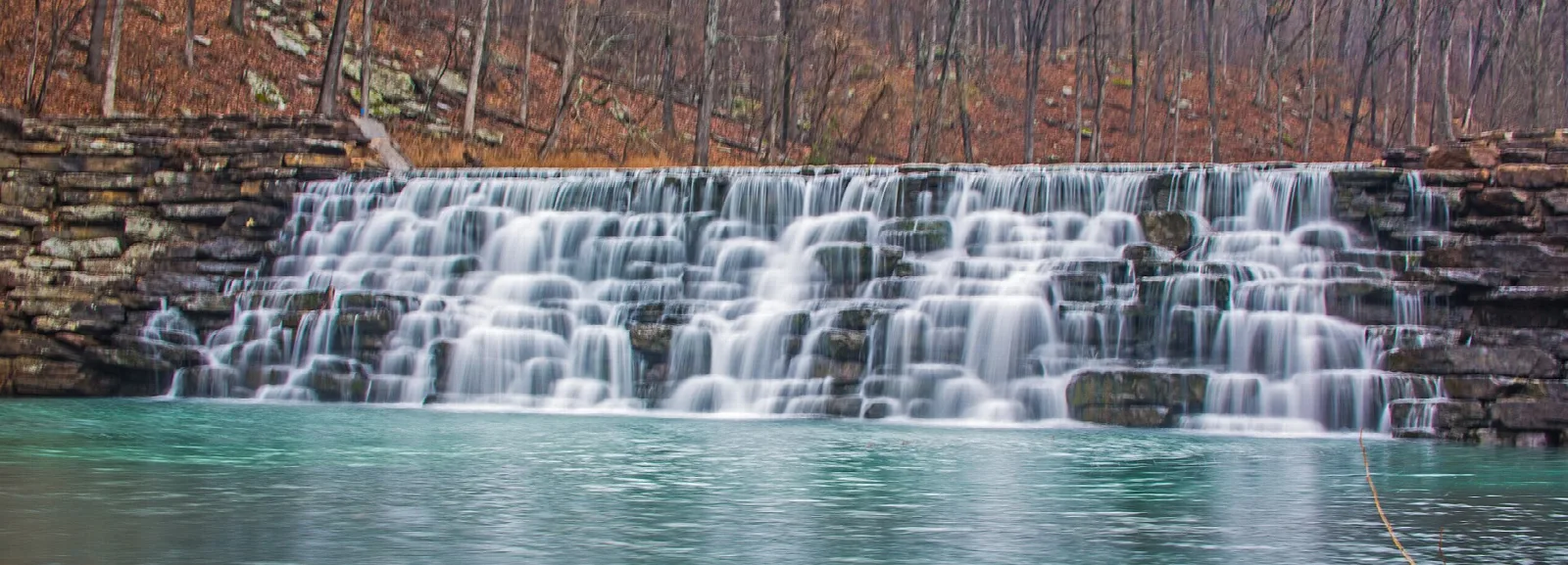 Wide low waterfall over a stone dam into a turquoise pool
