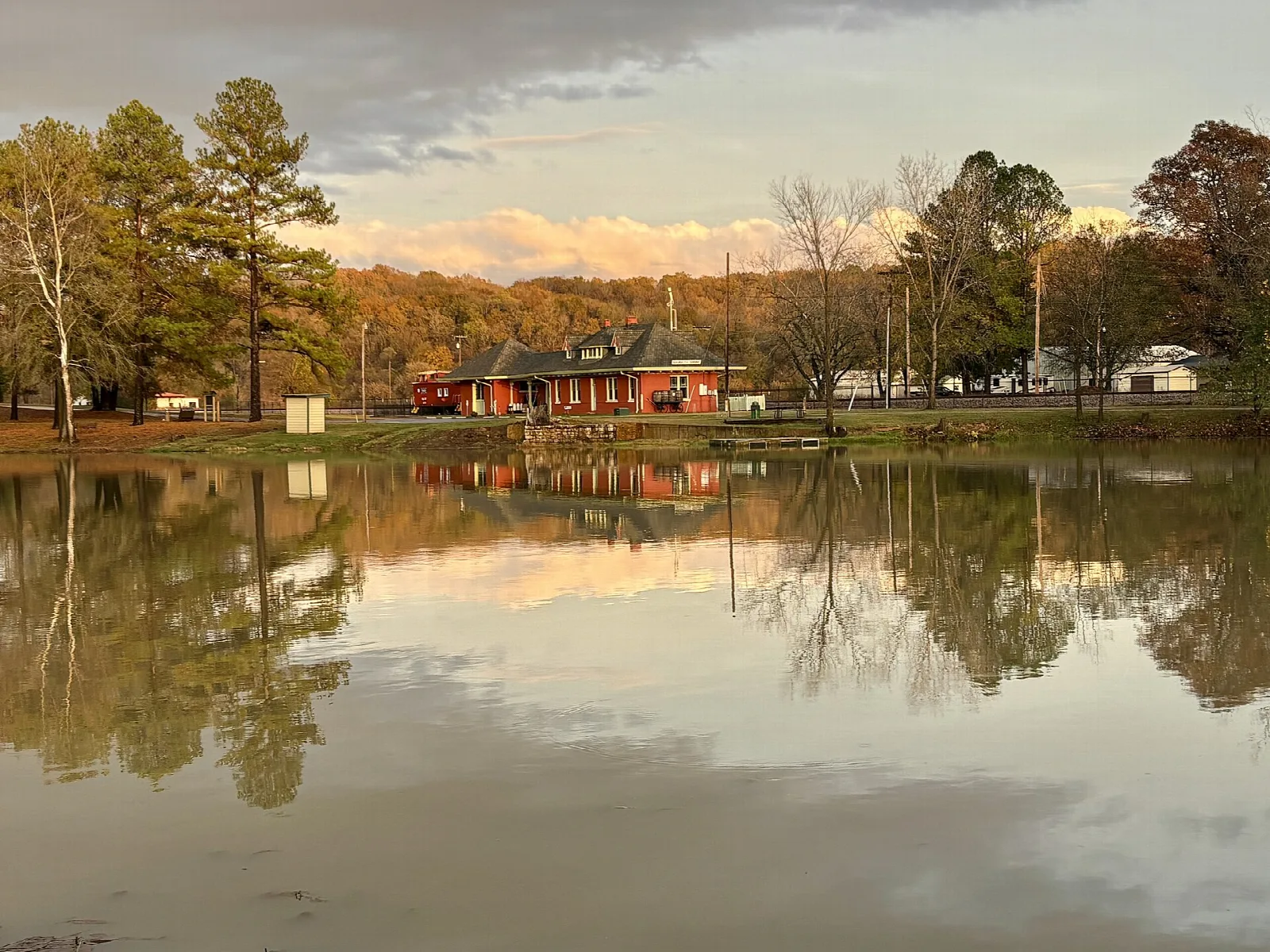 Red train depot across still water at sunset with trees reflected in the surface