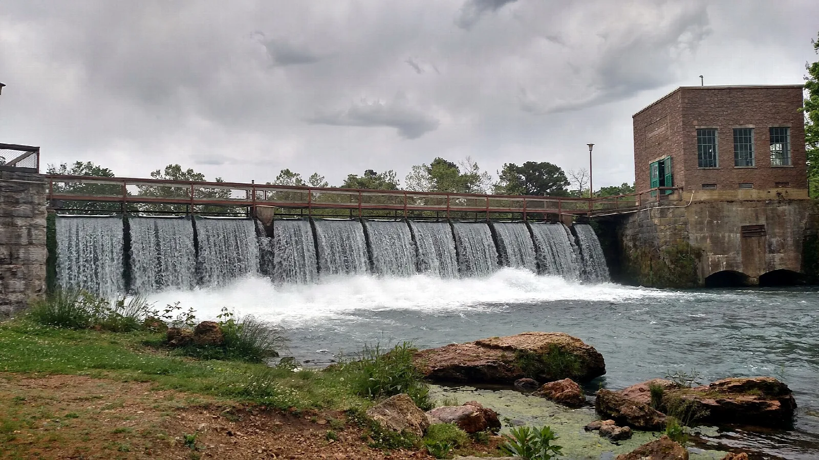 Low spillway with water pouring over it beside a brick building
