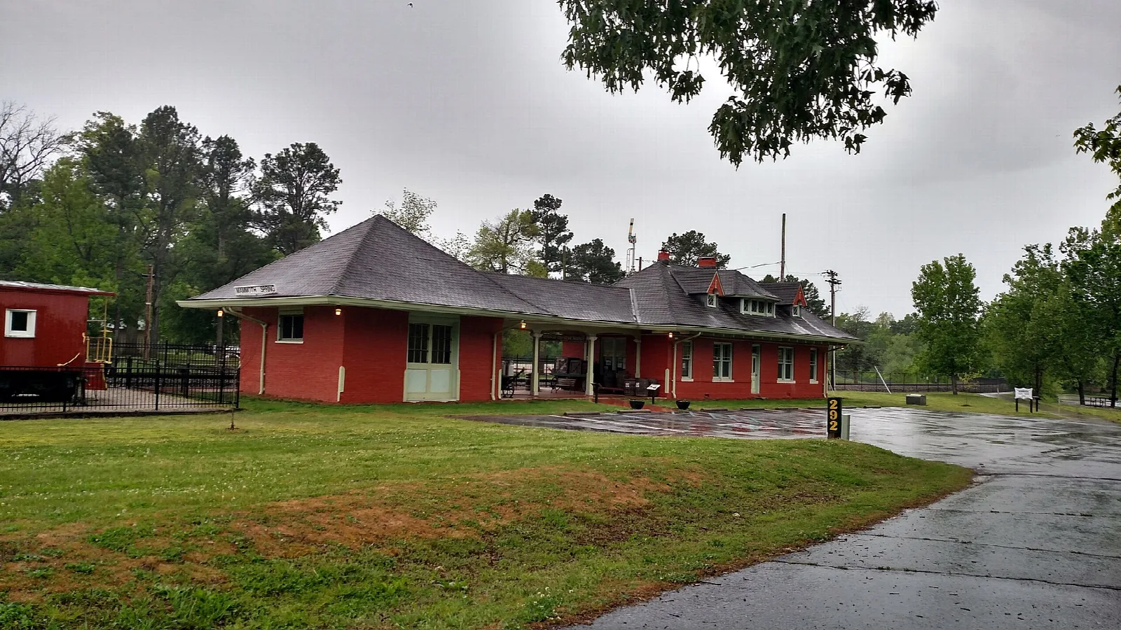 Red depot building with a wide roof on a green lawn