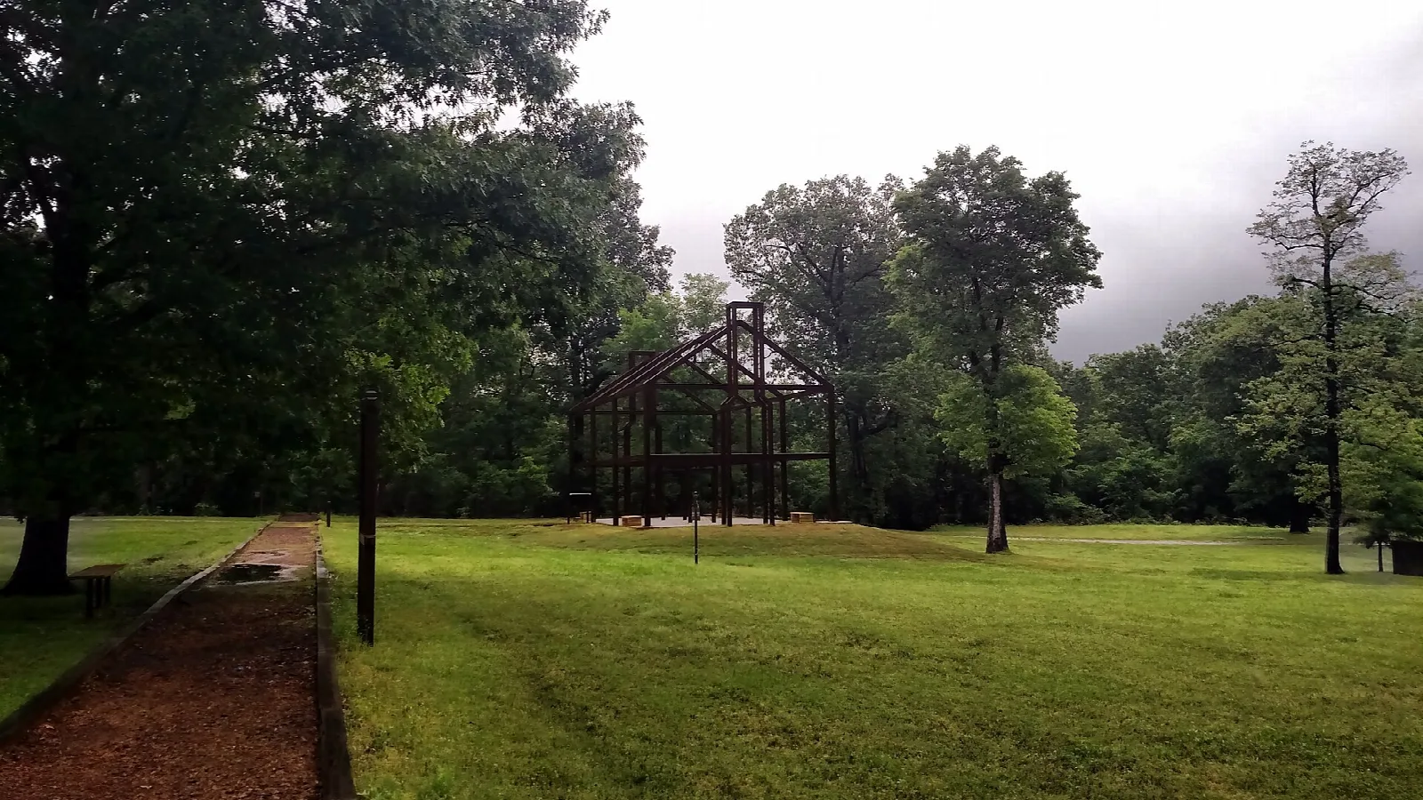 Open lawn with a distant steel building frame and a brick path under cloudy sky
