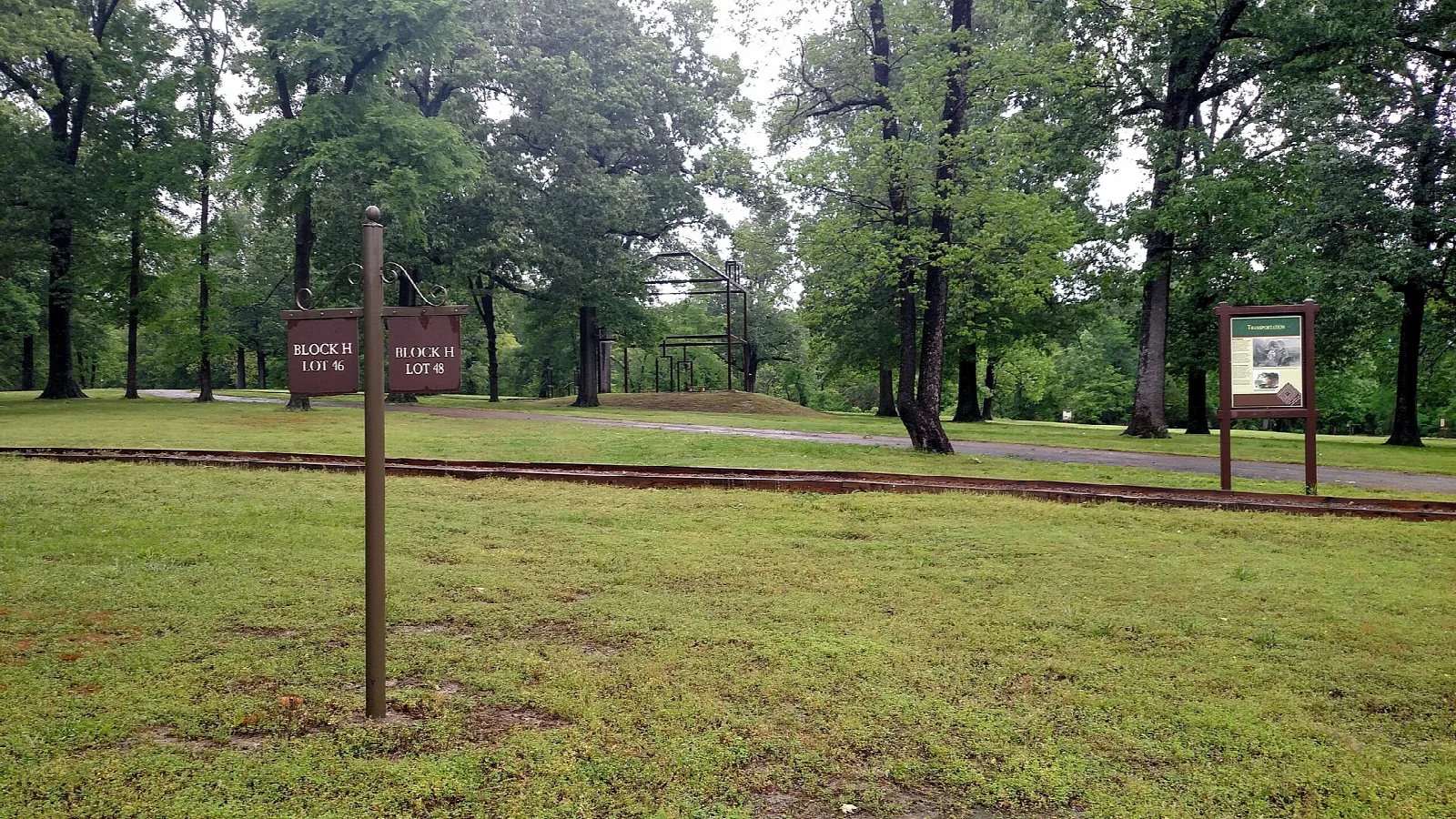Grassy townsite among trees with an interpretive sign beside a brick-edged path