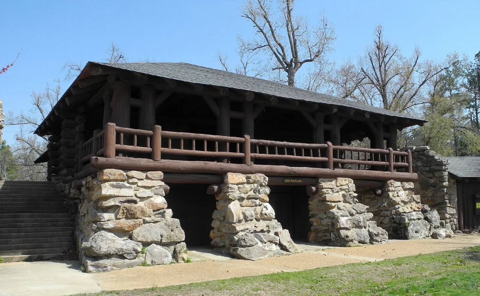 Log and stone pavilion with a wooden railing on a green lawn