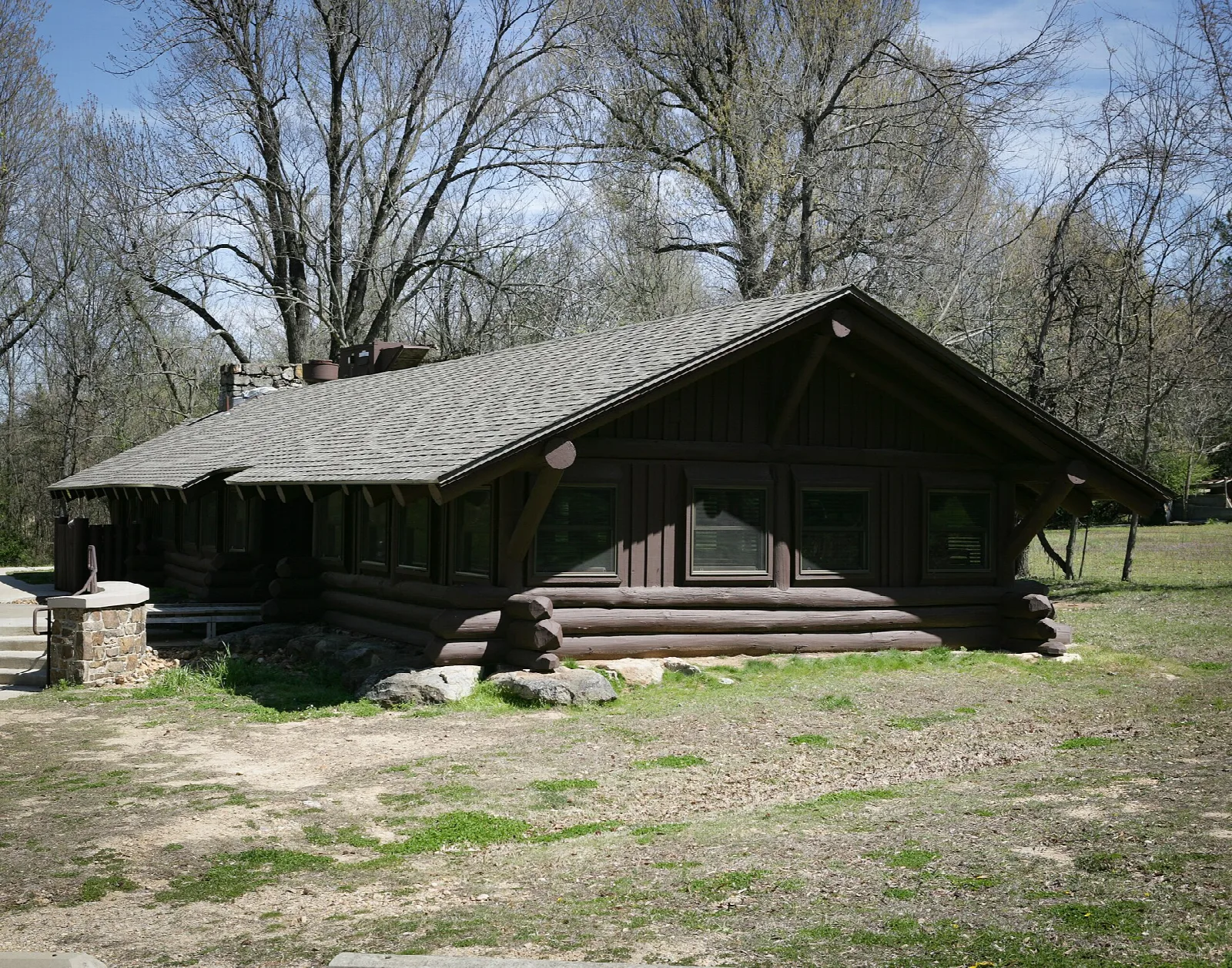 Dark log dining hall with a stone chimney among bare trees