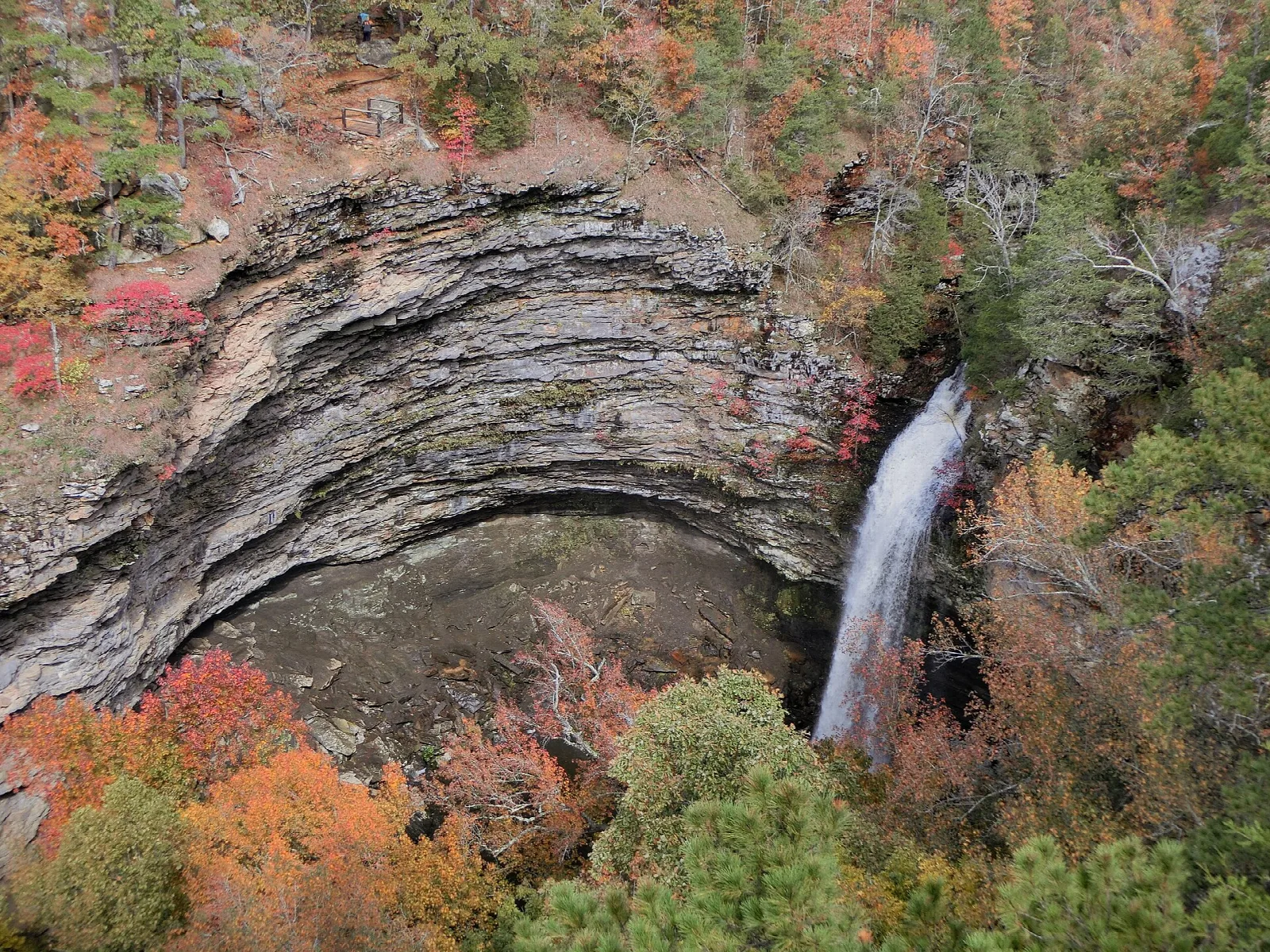 Waterfall dropping into a round rock canyon ringed by fall color