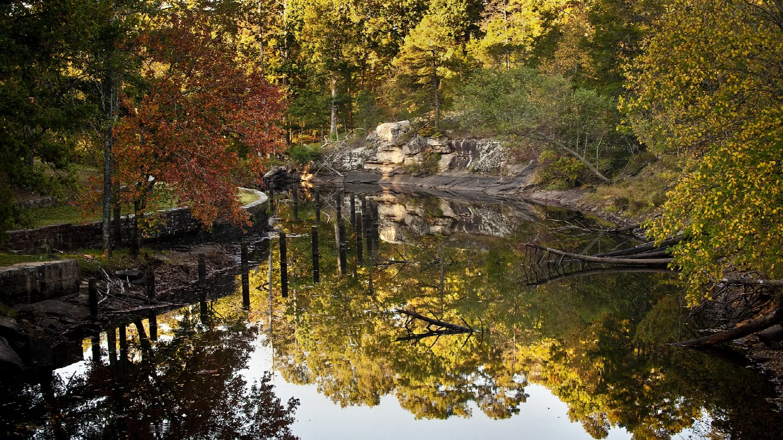 Still water with autumn trees reflected beside a rock bank