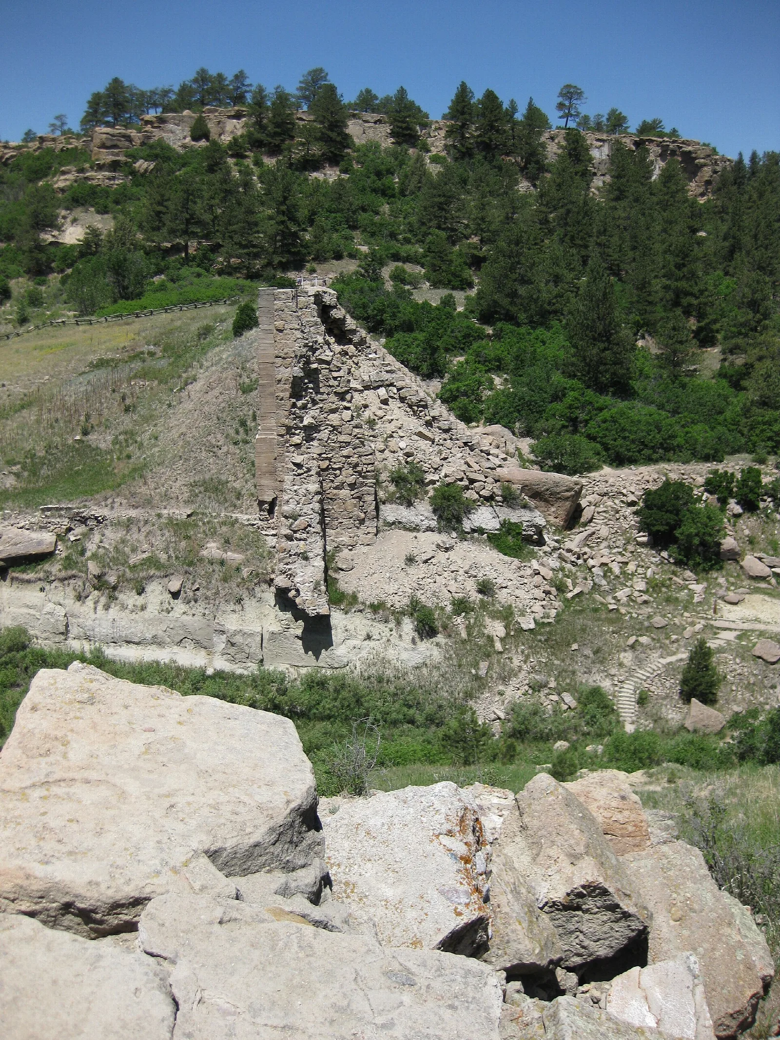 Weathered stone remains of a dam among pine-covered hills