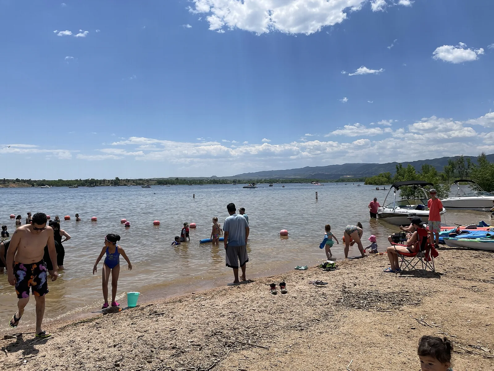 A sandy swim beach with people at the water's edge and hills in the distance