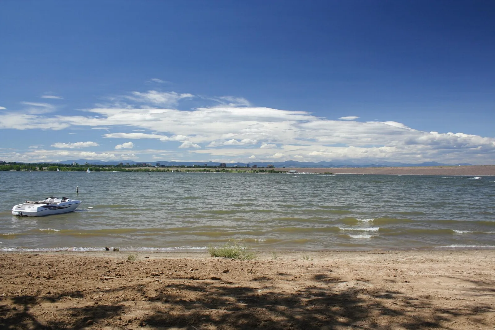 A boat anchored near a sandy shore on a wide lake under blue sky