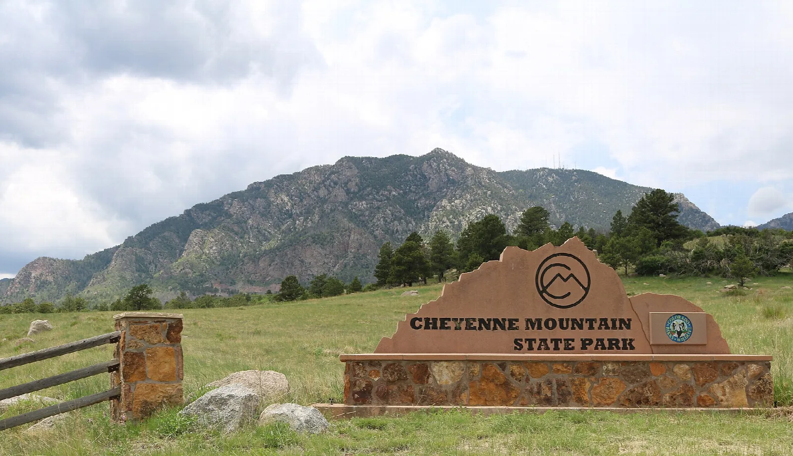 Stone park entrance sign in a grass meadow with a rocky mountain behind