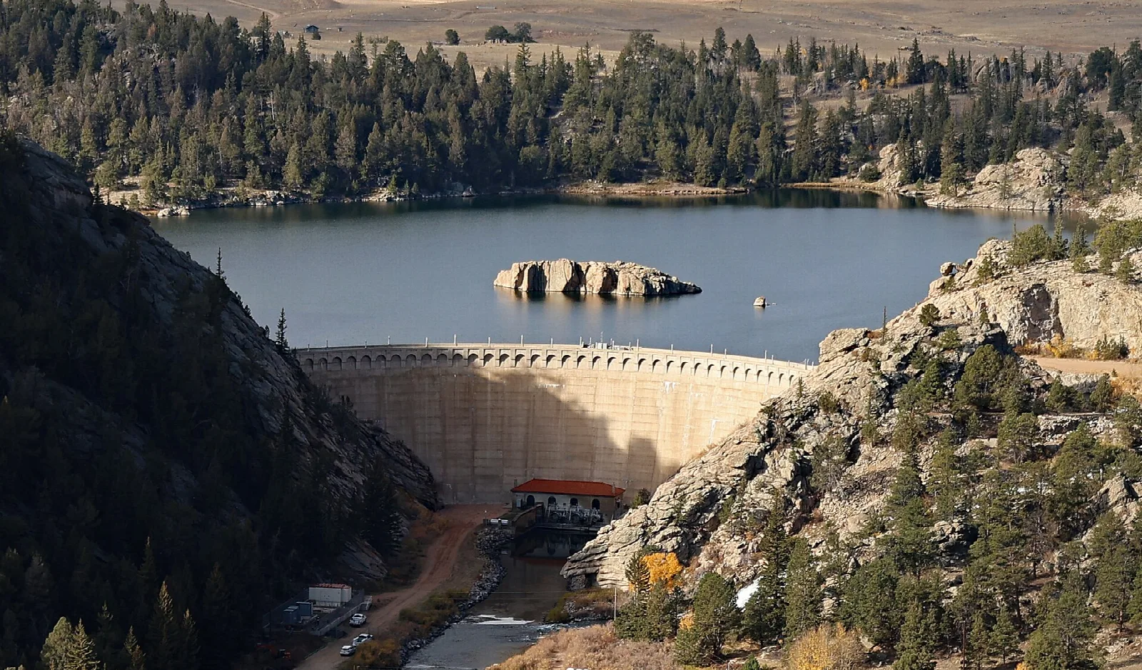 A concrete dam holding back a reservoir among pine forest