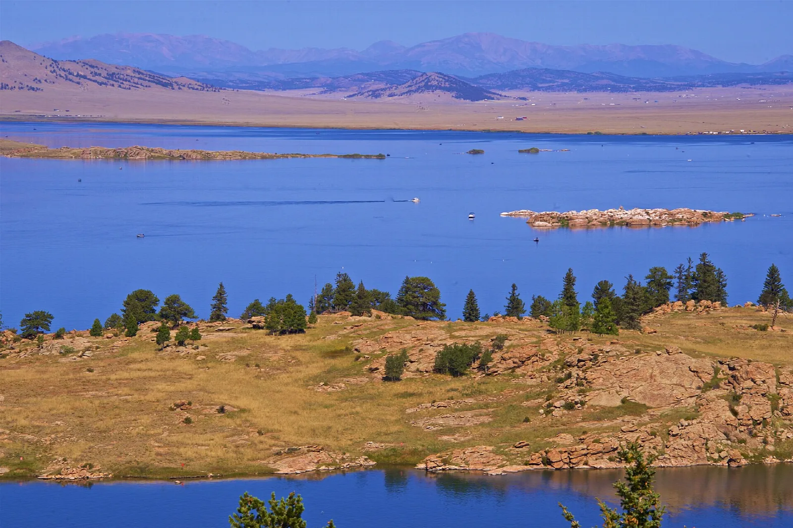 Blue reservoir with a grassy point and mountains in the distance