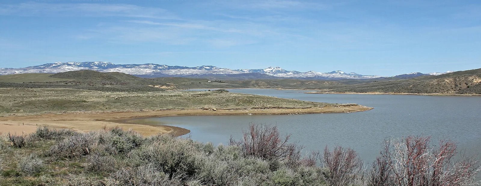 A wide reservoir with sagebrush in front and snowy hills far behind