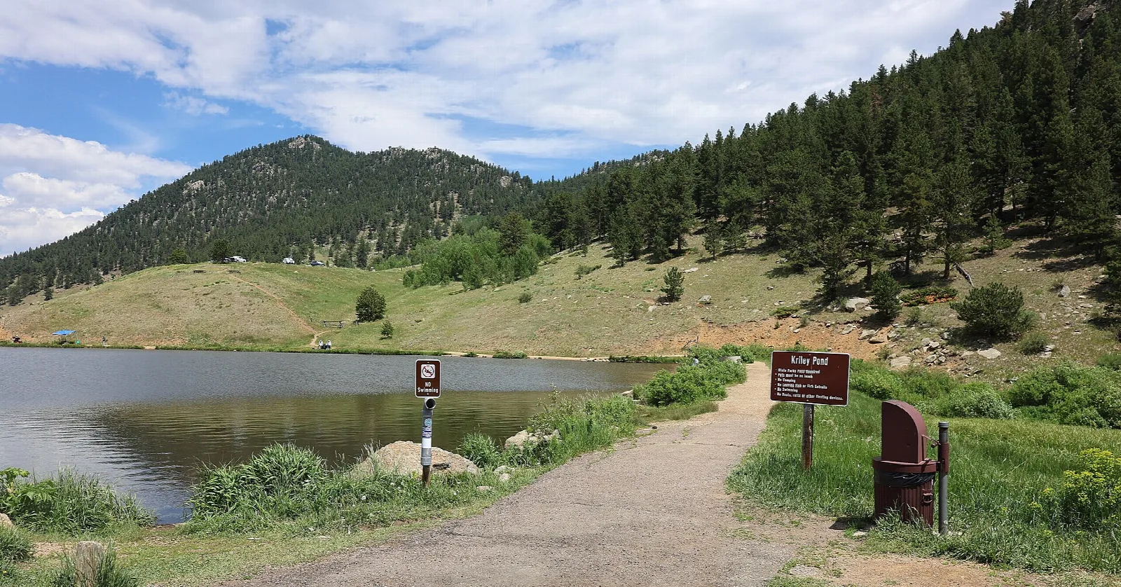 A pond below a grassy hill with a path alongside