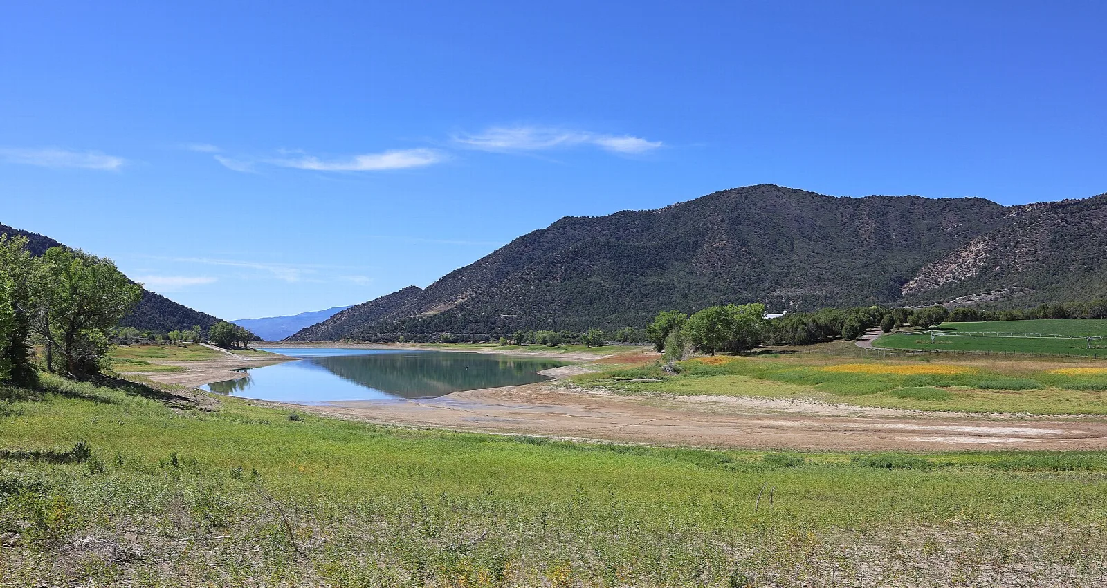 A reservoir with a sandy shore and green hills below a dark ridge