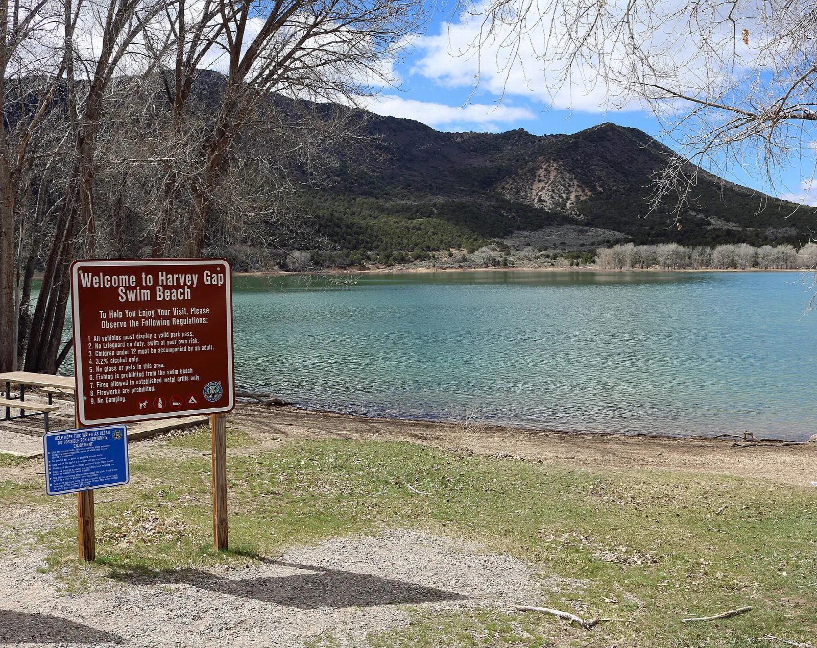 A turquoise reservoir with a beach sign and mountain slopes behind