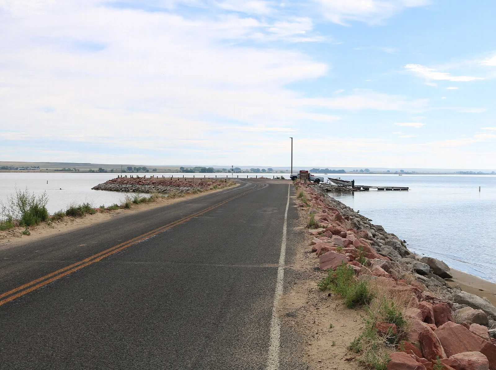 Paved road running beside a rocky shoreline and open water under a wide sky