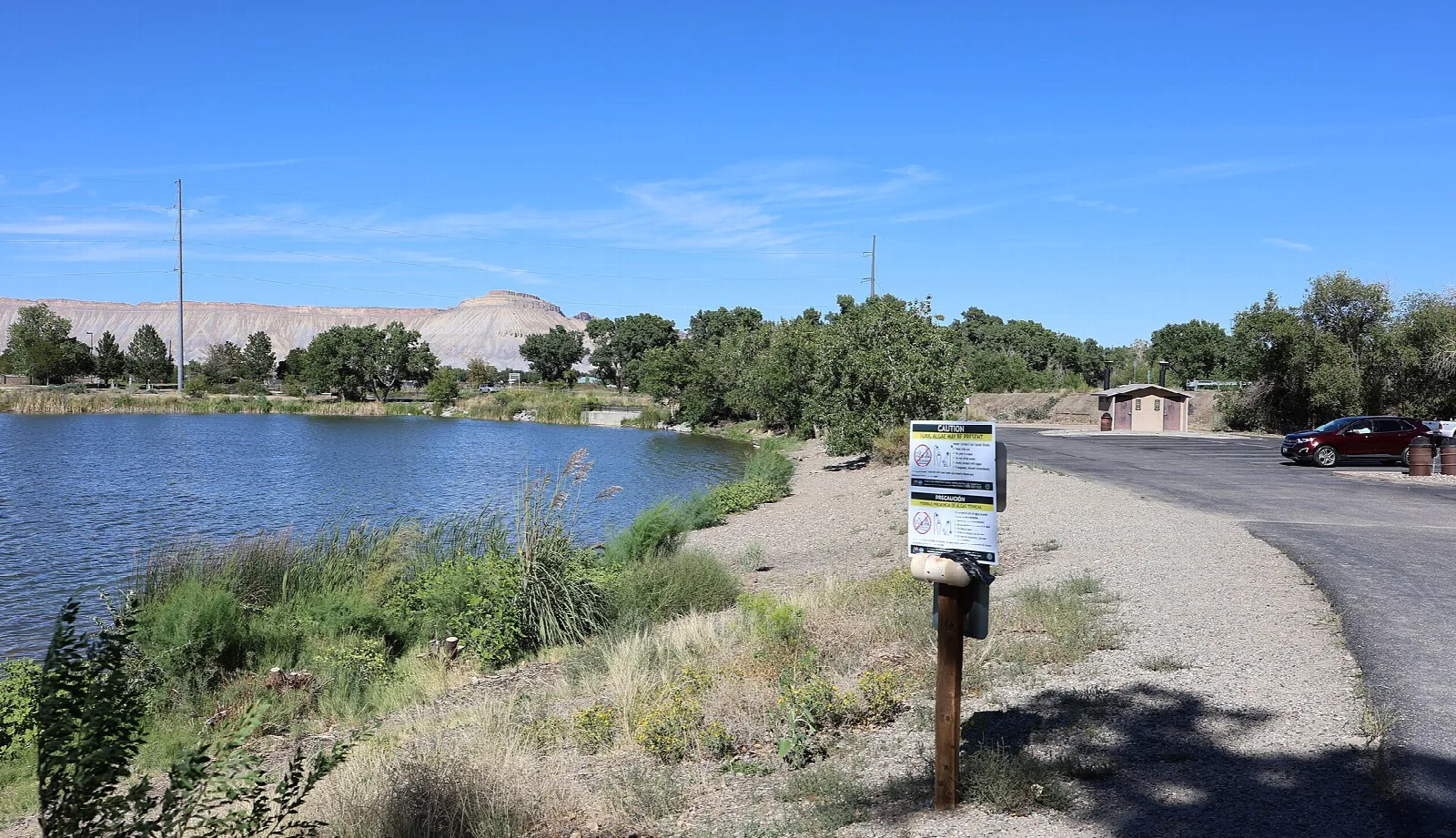 Blue lake with a gravel path, cottonwoods and a bluff in the distance