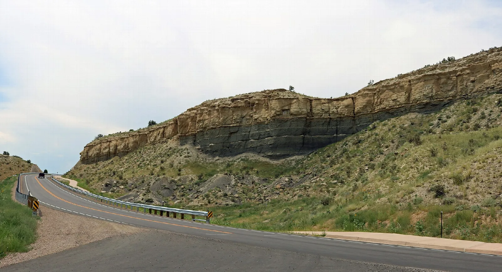 Winding road below a layered sandstone cliff