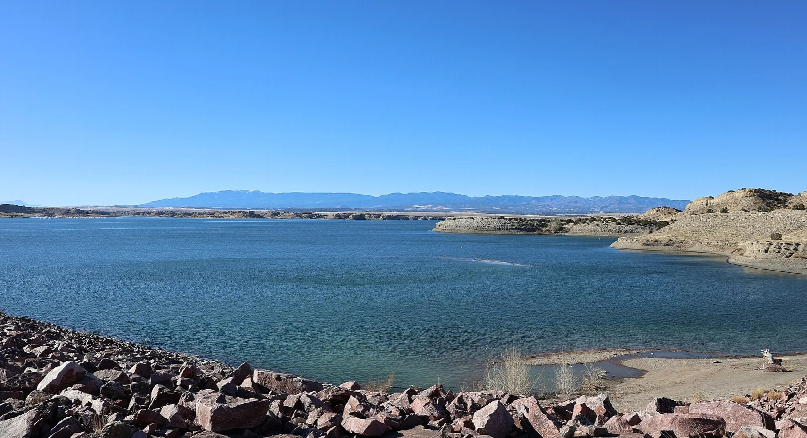 Blue lake and rocky dam shoreline with mountains in the distance