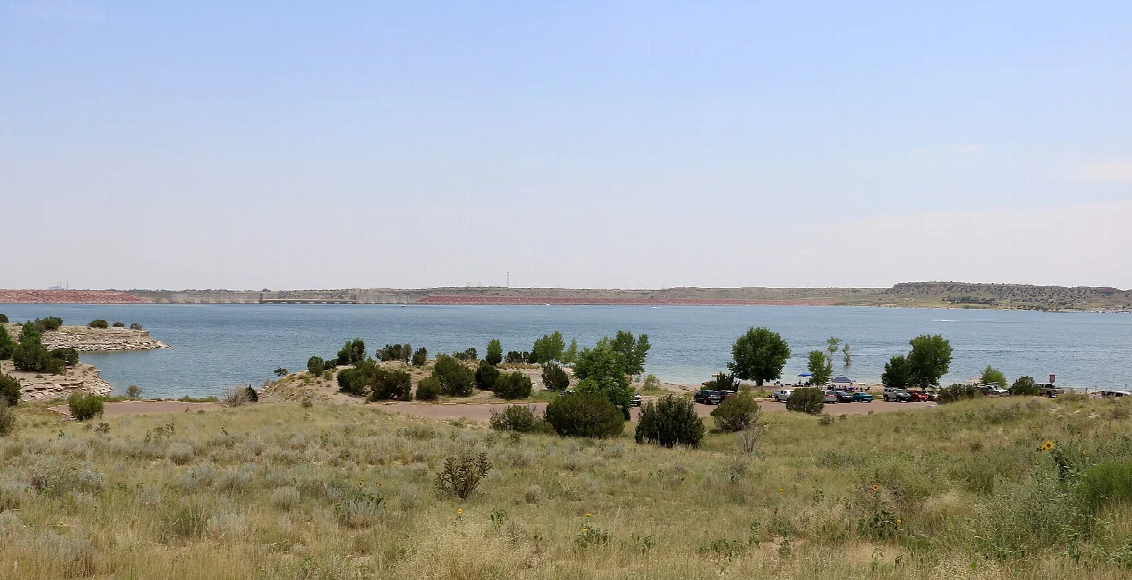 Wide lake with shrubs on the near shore and distant mesas