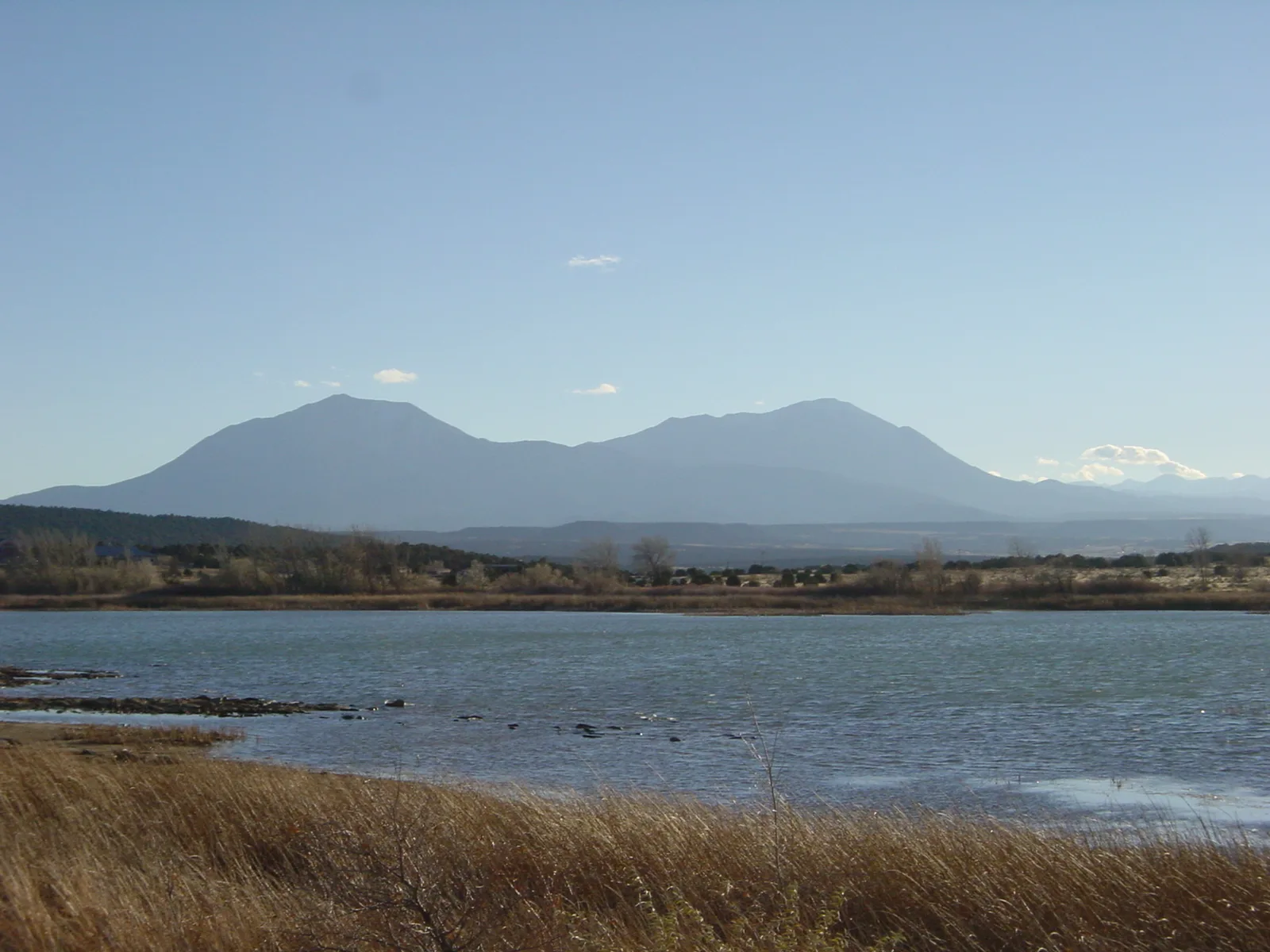 Two-peaked mountain across a lake with tall dry grass in front