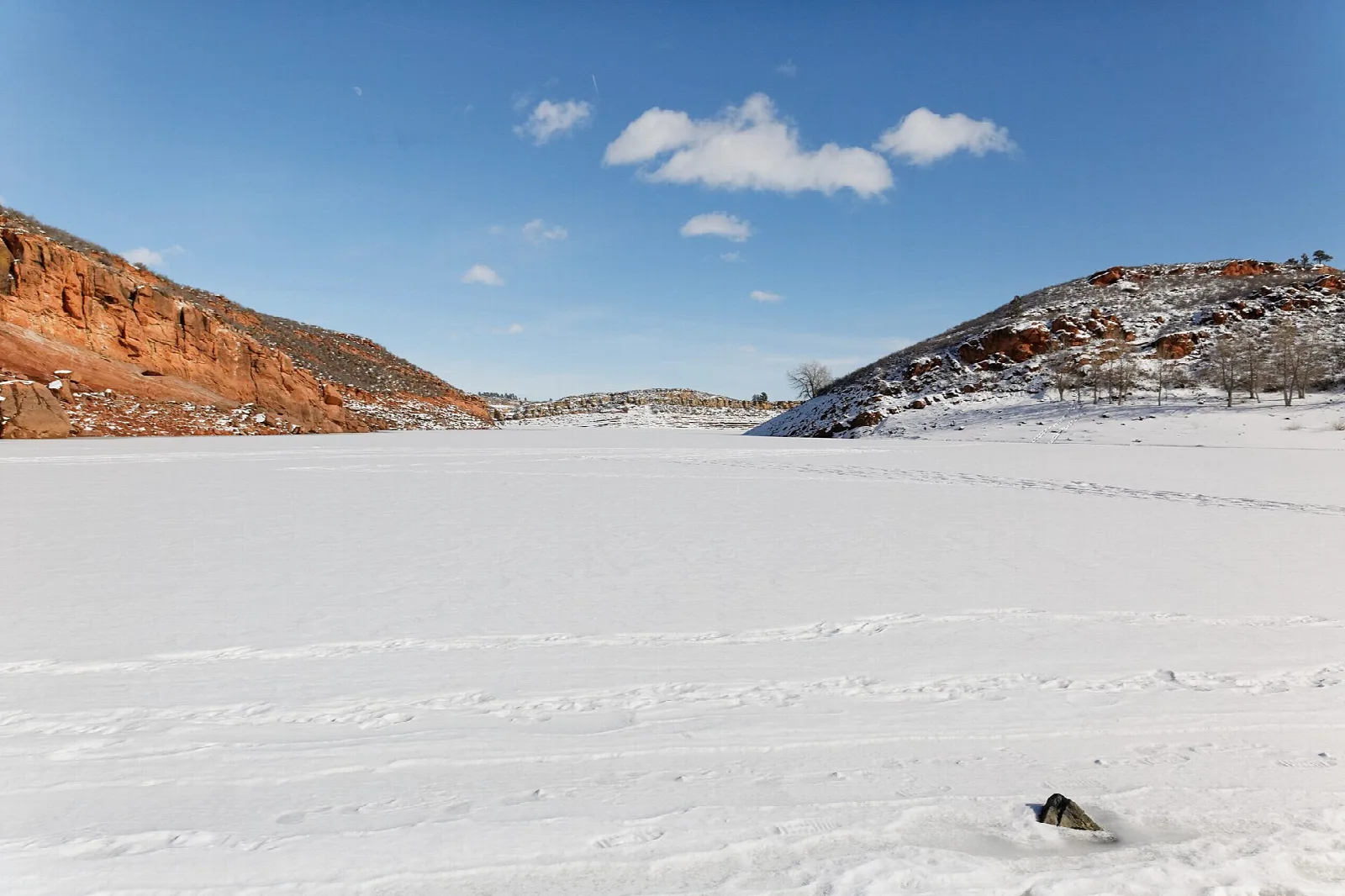 Flat snow-covered ground below red rock hills under blue sky