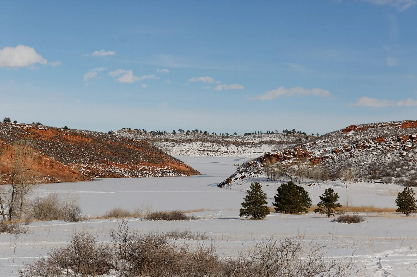 Snowy flat valley with red rock hills and a few pines