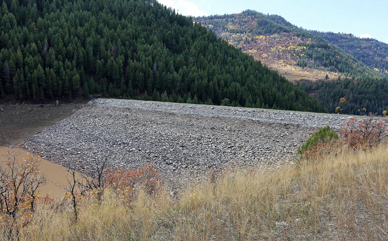 Rock dam beside a reservoir with dark conifer slopes behind