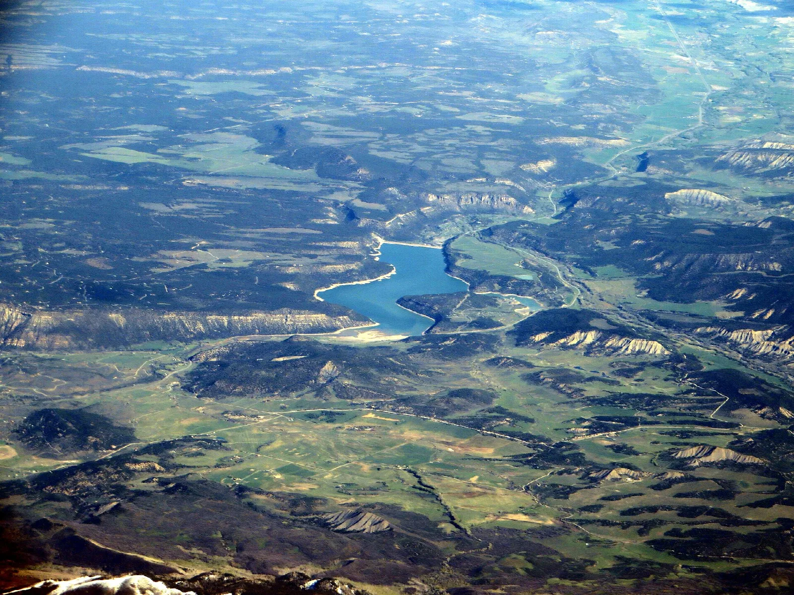 Aerial view of a blue reservoir winding through green valleys